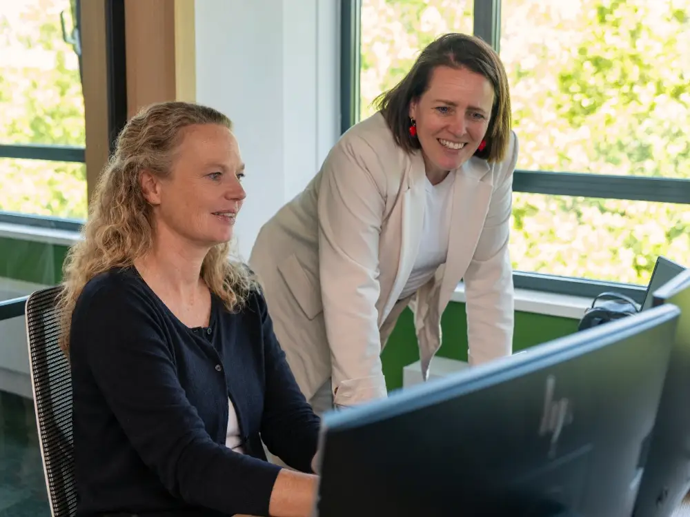 Twee collega's bekijken samen iets op een beeldscherm op kantoor