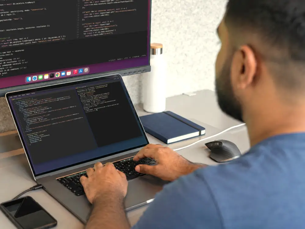 Ontwikkelaar werkt aan code op een laptop met een tweede beeldscherm